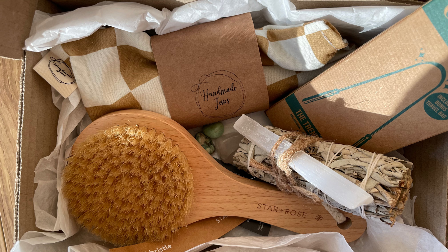 Box containing a wooden brush, incense sticks, and other items with branding on a textured surface.