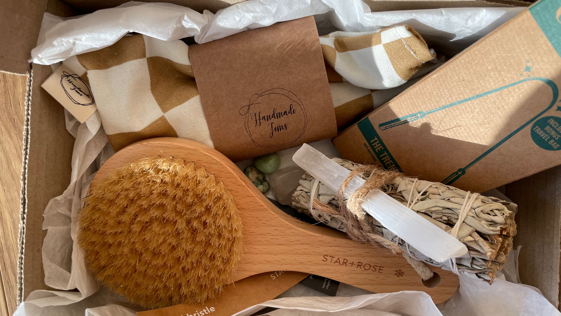 Box containing a wooden brush, incense sticks, and other items with branding on a textured surface.